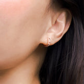 Fine jewellery, silver jewellery plated with rose gold, hypoallergenic, tarnish-free, close-up right view of a Rose gold hoop earrings with embedded crystals worn on a person's ear